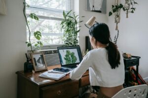 Woman working on a laptop in a plant-filled home office, embodying a modern freelance lifestyle.
