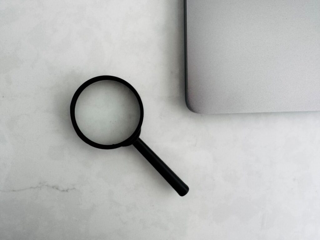 Magnifying glass beside the corner of a laptop on a marble surface
