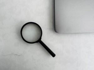 Magnifying glass beside the corner of a laptop on a marble surface