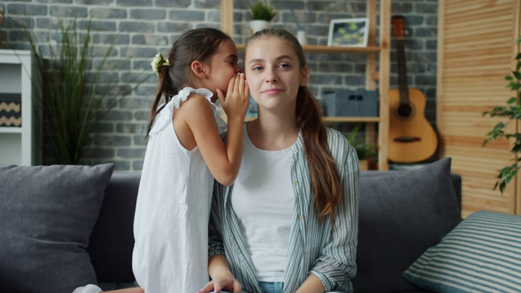 Adorable little girl is whispering secret in mother's ear smiling hugging expressing love, mom is enjoying closeness to child. People and family concept.