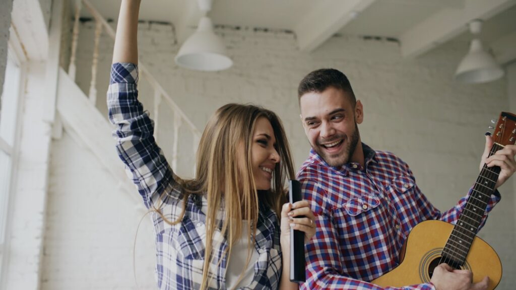 Funny happy and loving couple dance on bed singing with tv controller and playing guitar. Man and woman have fun during holiday at home