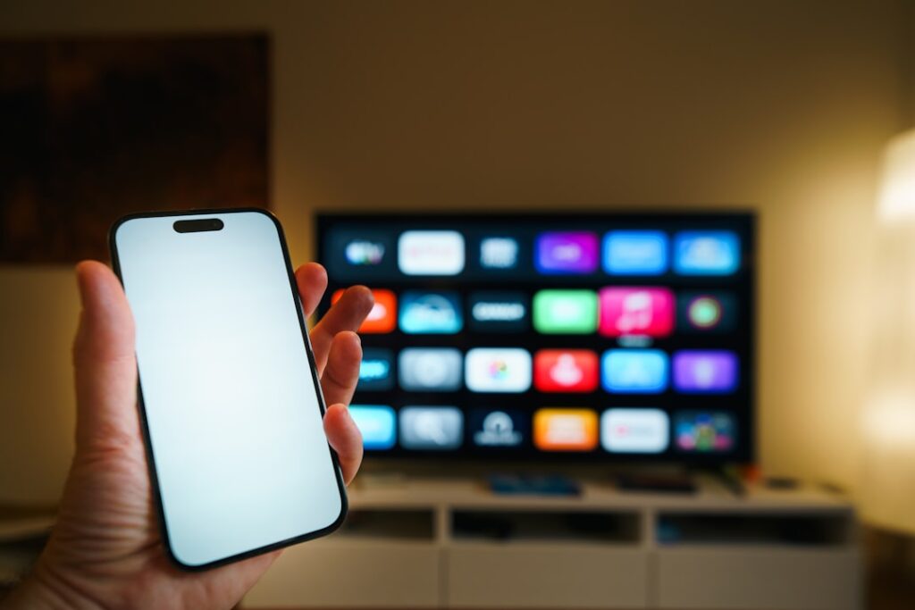 Streaming platforms home entertainment smartphone blank screen mockup television. Hand holding modern mobile device empty display foreground large smart television interface background living room interior technology lifestyle media consumption editorial concept