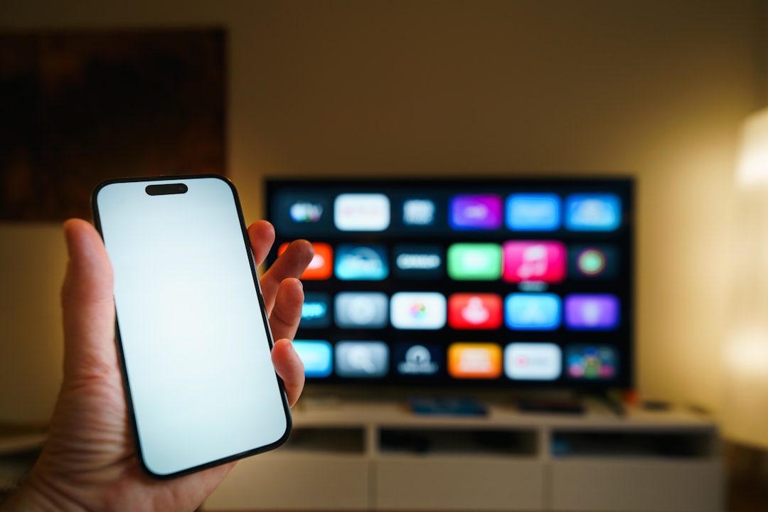 Streaming platforms home entertainment smartphone blank screen mockup television. Hand holding modern mobile device empty display foreground large smart television interface background living room interior technology lifestyle media consumption editorial concept