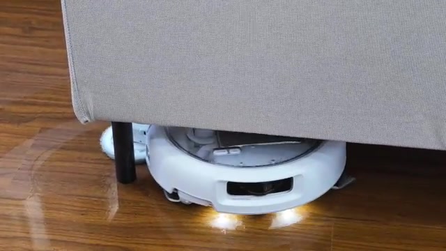 Robotstofzuiger met verlichting rijdt onder een bank door over een houten vloer
